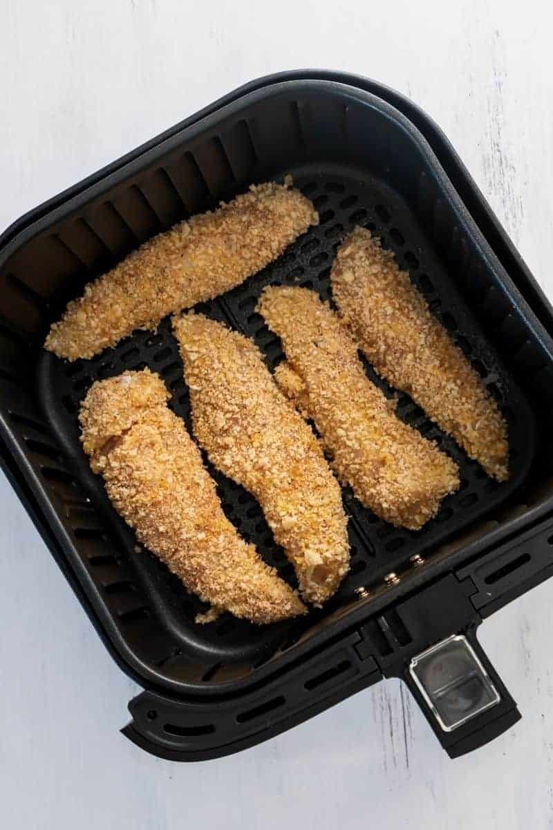 Closeup picture of breaded chicken tenders with parsley on top on a white plate