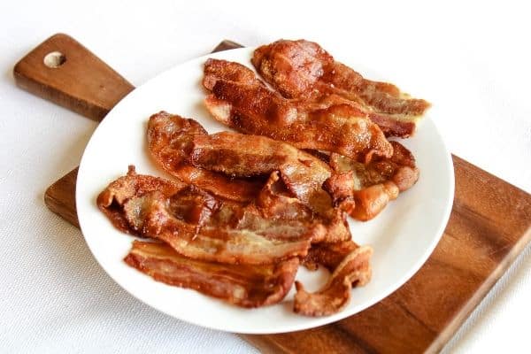 Crispy Air Fryer Bacon on a white plate with small brown cutting board