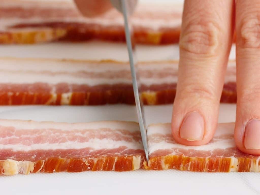 Cutting  raw bacon in half with a knife