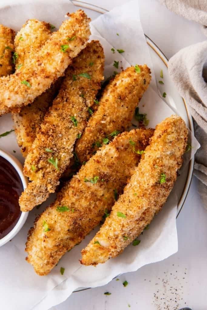 Panko breaded air fryer chicken strips on a serving plate with bbq sauce