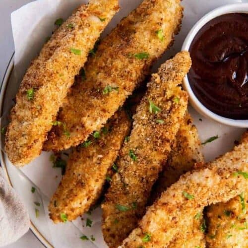 Breaded air fryer chicken tenders with buffalo sauce and parsley on top (on a white plate)