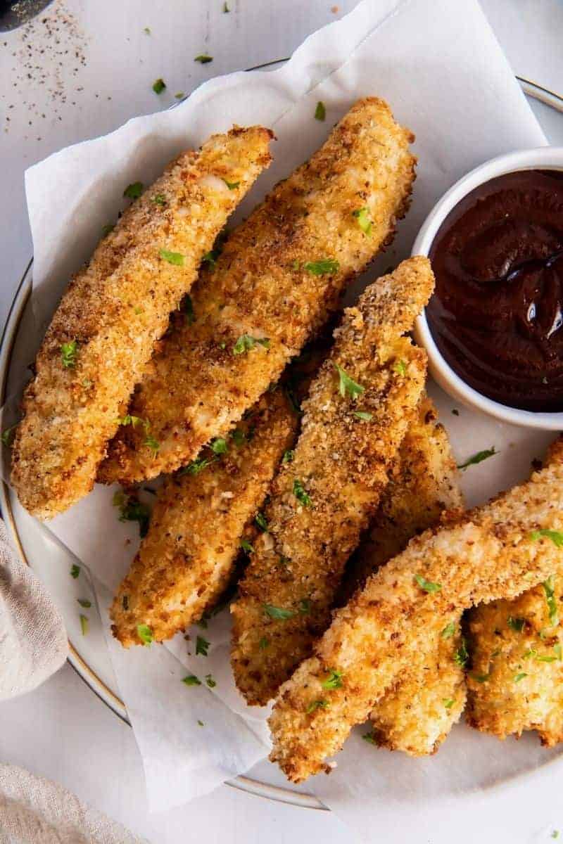 Breaded air fryer chicken tenders with buffalo sauce and parsley on top (on a white plate)