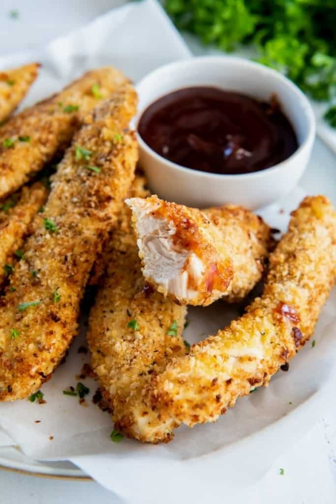 Chicken tenders with a bite taken out served with bbq sauce