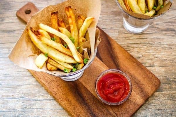 French Fries in bowl with paper on a cutting board with small bowl of ketchup on side