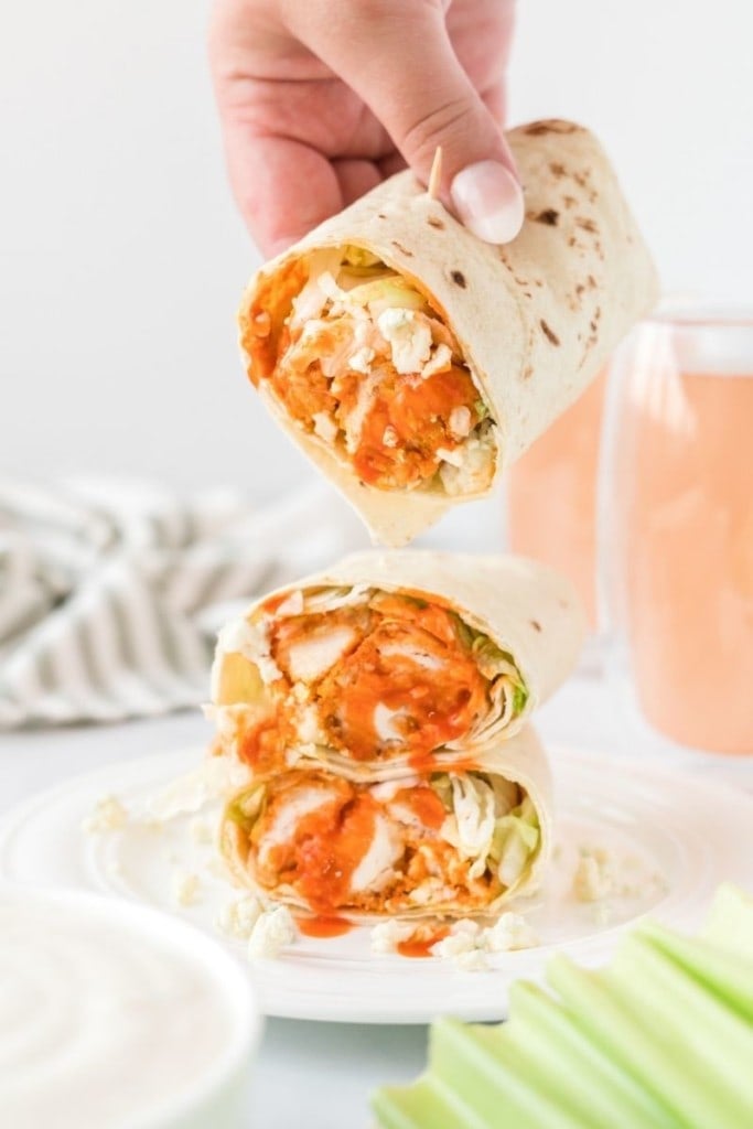 Homemade buffalo chicken wraps stacked on each other with a hand pulling off the top one