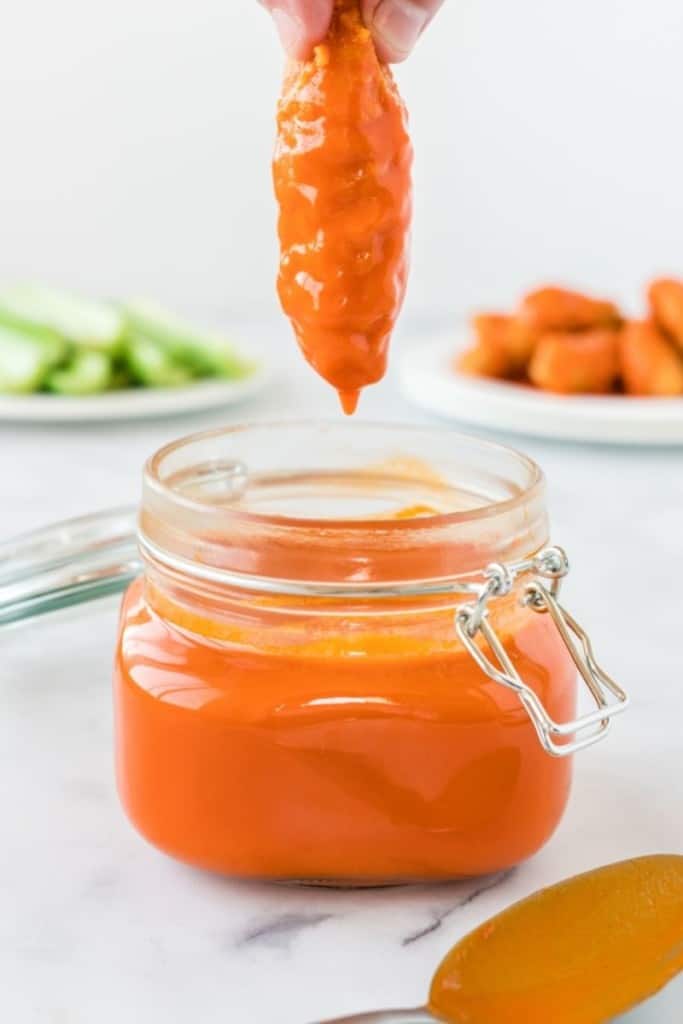 Piece of breaded chicken tender being dipped into the buffalo sauce