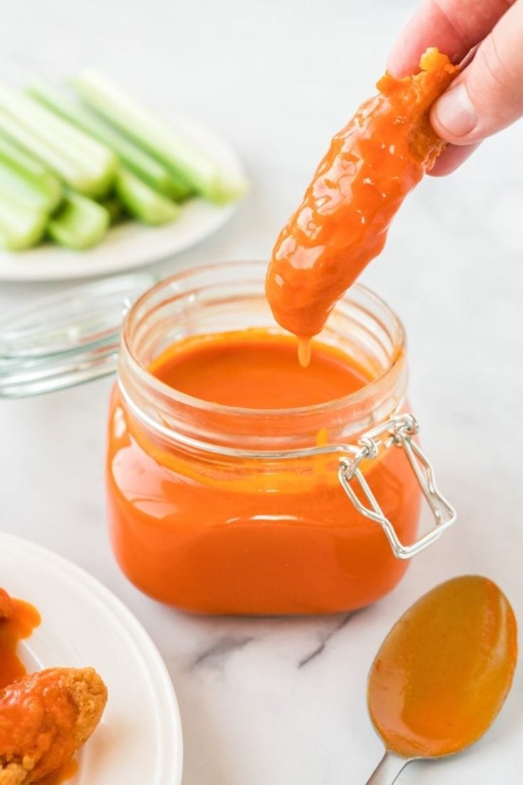 Homemade Buffalo Sauce in a mason jar with chicken tender being dipped in them