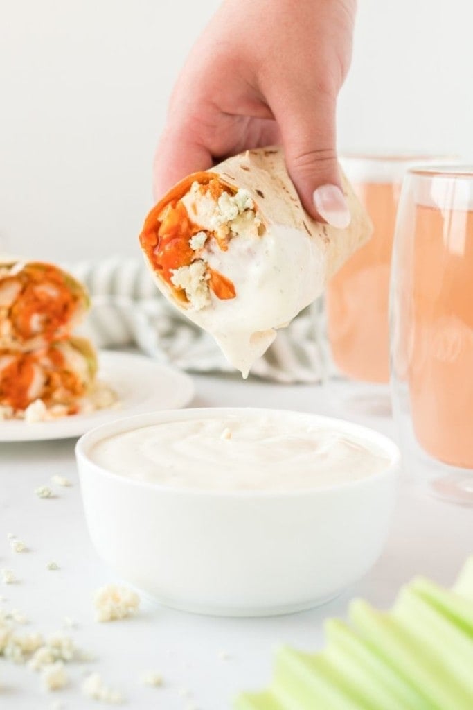 Homemade buffalo chicken wrap being dipped into a white bowl of blue cheese