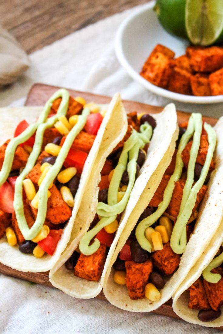 Sweet Potato Black Bean Tacos served on a rectangular wooden tray topped with avocado crema