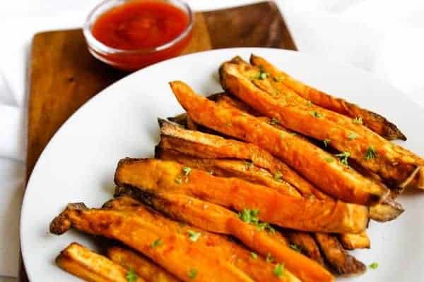 Air Fryer Sweet Potato Fries on a white plate with ketchup bowl in back