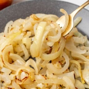 Closeup on sauteed onions on a plate with a fork picking some of them up