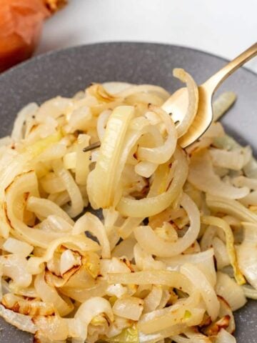 Closeup on sauteed onions on a plate with a fork picking some of them up