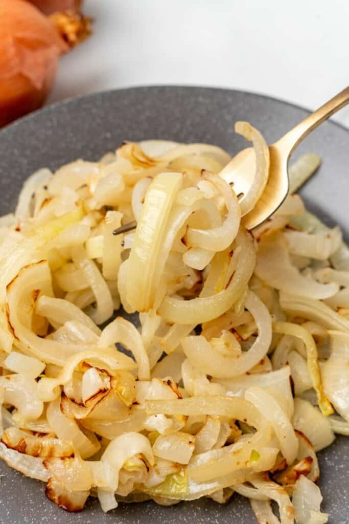 Closeup on sauteed onions on a plate with a fork picking some of them up