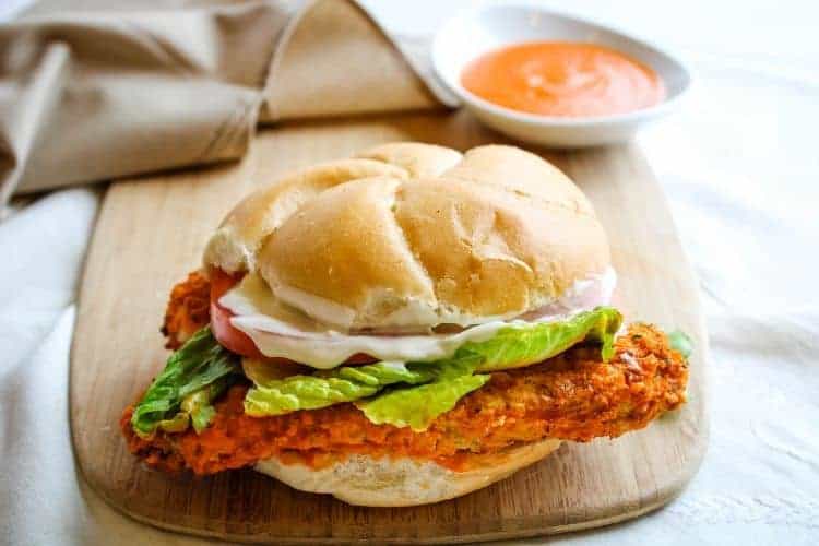 Buffalo Chicken Sandwich on cutting board with buffalo sauce in background