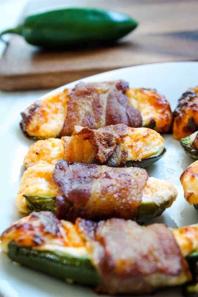 Air Fryer Bacon Jalapenos on a white plate with jalapeno pepper in background