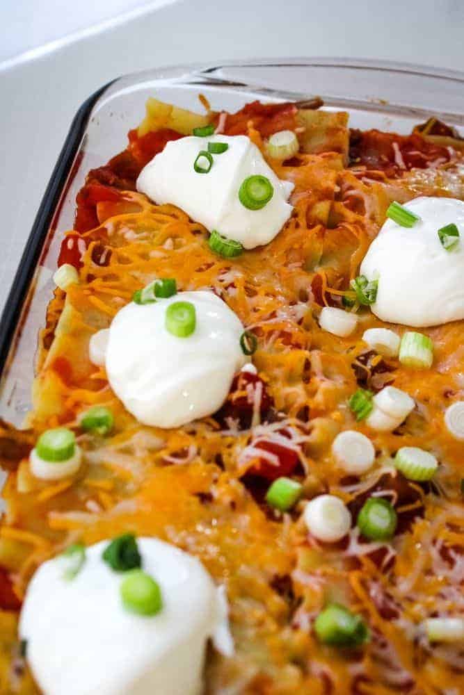 Taco Lasagna with sour cream and green onions on top in casserole dish
