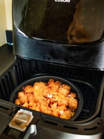 Cosori Air Fryer with drawer halfway open and a small pie plate with totchos inside