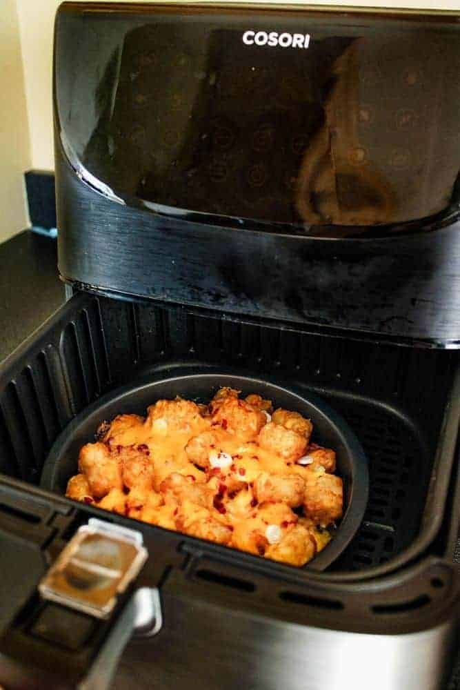 Cosori Air Fryer with drawer halfway open and a small pie plate with totchos inside.