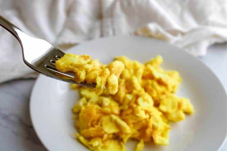 Scrambled Eggs on a fork with white plate in background