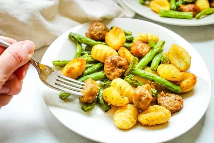 Air Fryer Sausage, Green Beans, and Gnocchi with hand holding a fork on a white plate