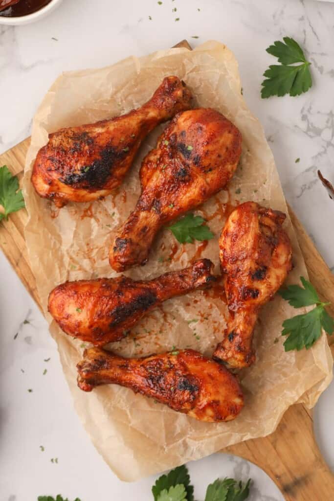 Overhead view of BBQ air fryer chicken drumsticks on brown parchment paper on top of a cutting board