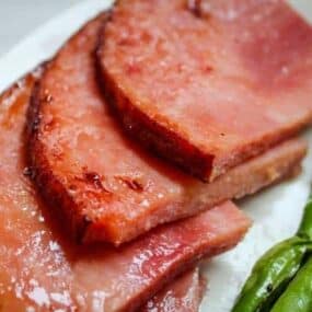 Air Fryer Ham Slices on a white plate with green beans in the corner