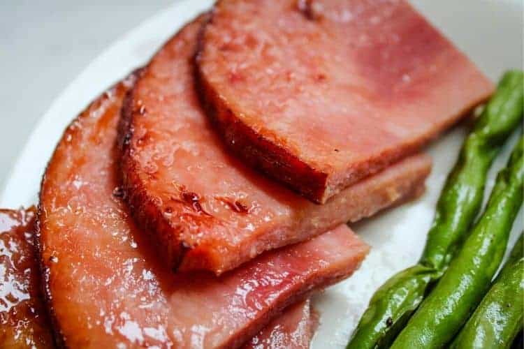 Air Fryer Ham Slices on a white plate with green beans in the corner