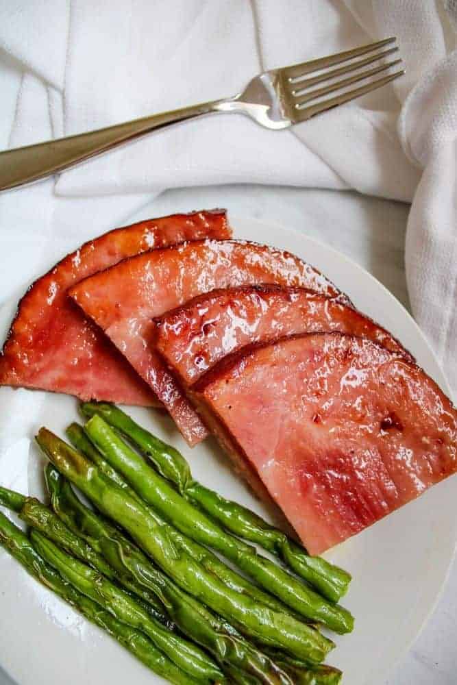 Ham Steaks with Green Beans on a white plate with fork over top of plate