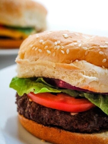 Closeup of Air Fryer Hamburger with lettuce and tomato on a sesame bun on a white plate