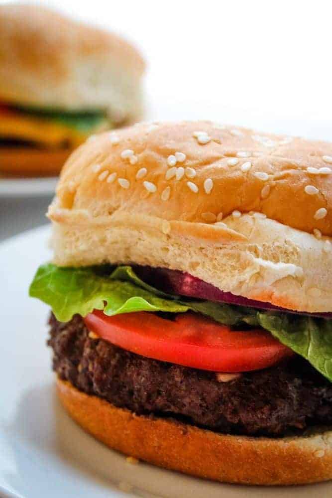 Closeup of Air Fryer Hamburger with lettuce and tomato on a sesame bun on a white plate