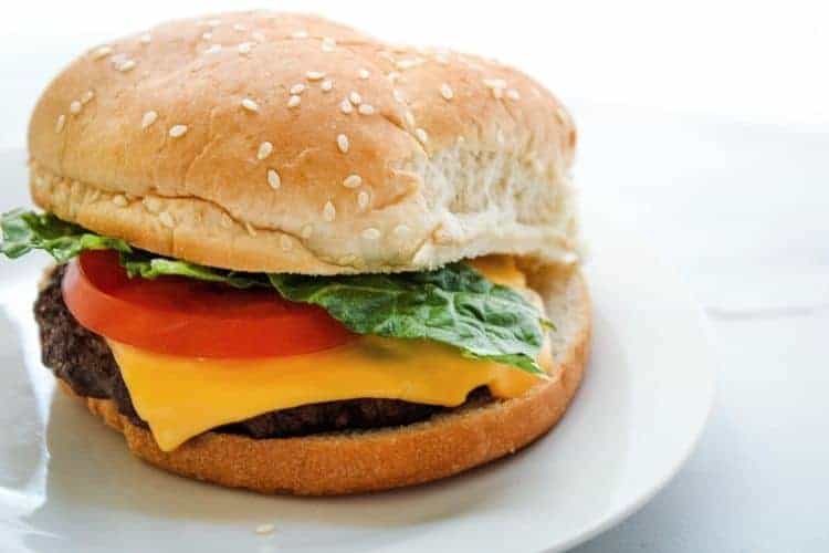 Air Fried Cheeseburger with lettuce and tomato on a sesame bun on a white plate