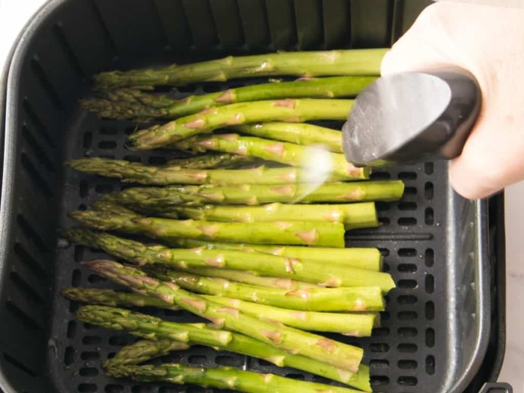 Asparagus in air fryer basket being sprayed with evo oil sprayer
