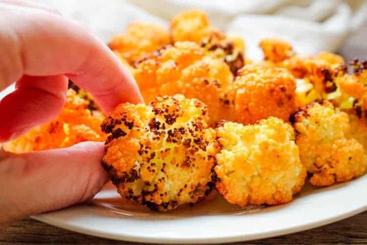 Air Fryer Buffalo Cauliflower with hand touching one of the florets