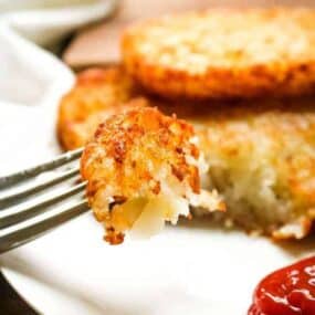 Closeup of a bite of crispy air fryer hash brown patties on a fork with ketchup to the side