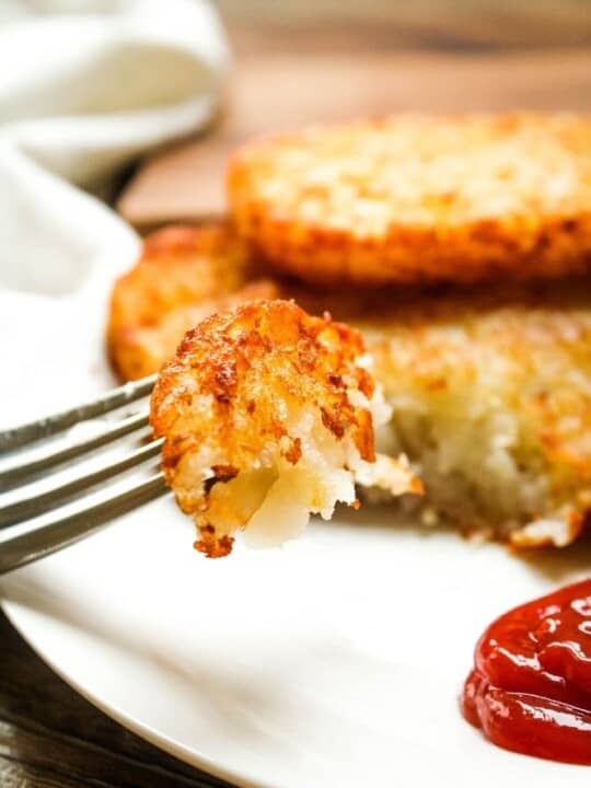 Closeup of a bite of crispy air fryer hash brown patties on a fork with ketchup to the side