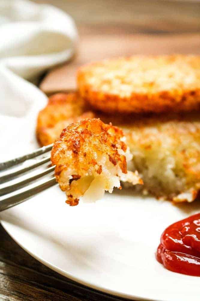 Closeup of a bite of crispy air fryer hash brown patties on a fork with ketchup to the side