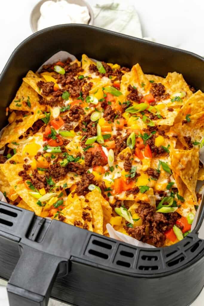 Nachos in air fryer basket with sliced green onions on top