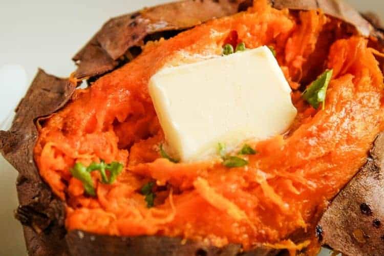 Closeup of baked sweet potato open on top with butter melting