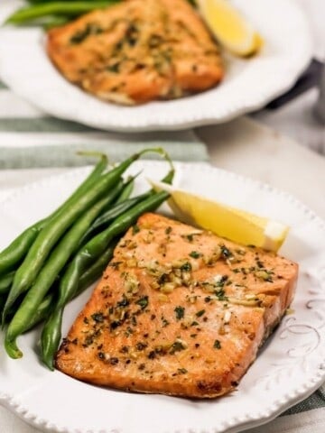 Vertical image of Air Fryer Garlic Salmon on a white plate with green beans and a lemon