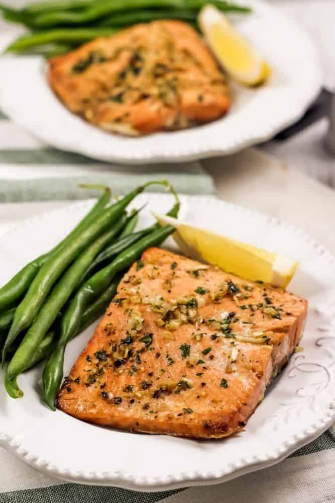 Garlic Butter Salmon on a white plate with green beans and a lemon