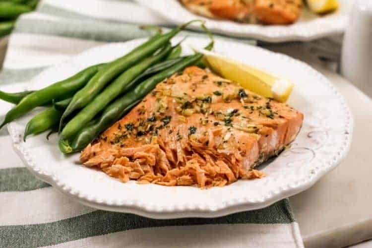 Garlic Butter Salmon that is shown flaking on a white plate with green  beans and a lemon