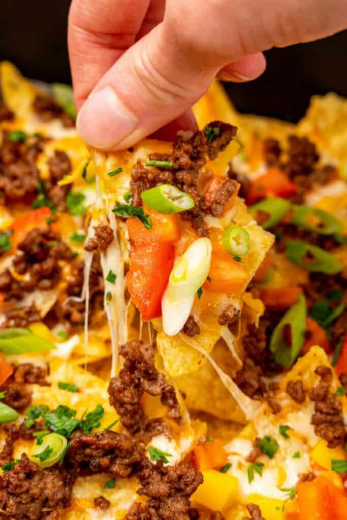 Loaded air fryer nacho being pulled from nachos with cheese attached