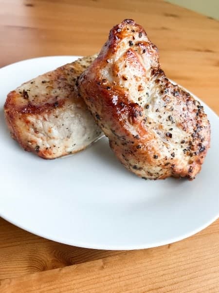 Two pork chops on  a white plate on top of a wood table