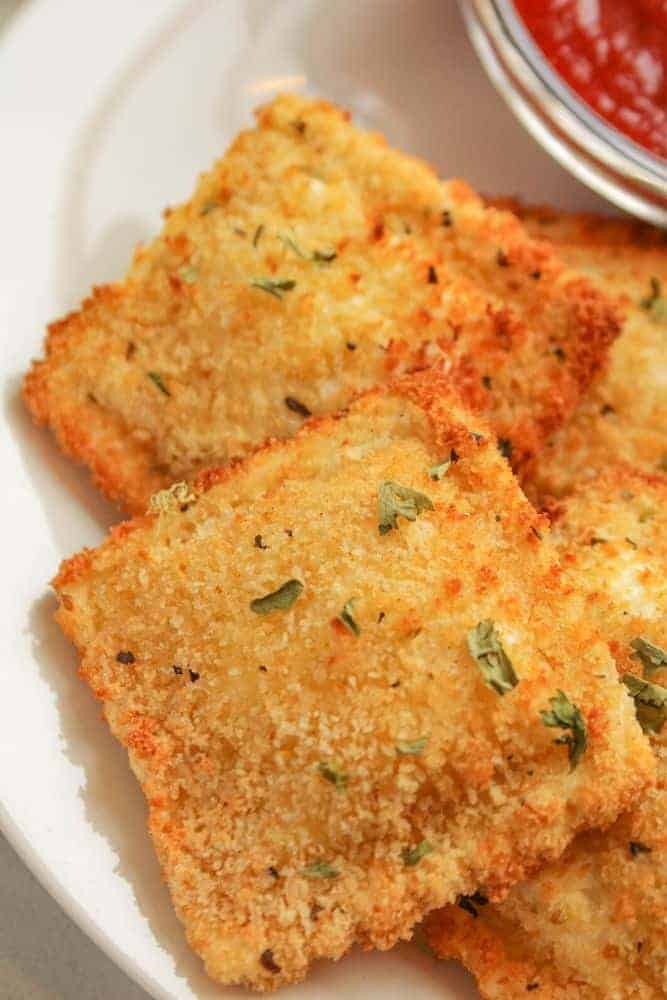 Air Fryer Ravioli on a white plate with marinara sauce in a bowl in the corner