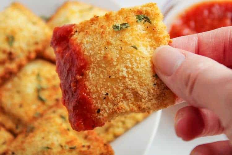 Hand holding an air fryer ravioli with sauce on it