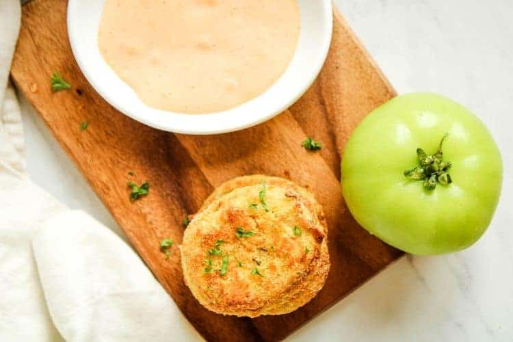 Overview shot of fried green tomatoes, whole green tomato, and sriracha mayo in a white bowl