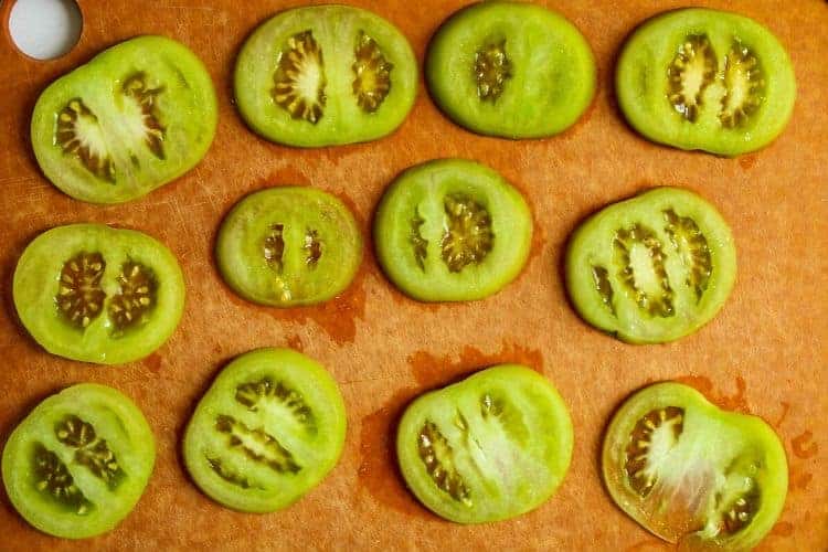 Sliced green tomatoes on a cutting board with salt on them