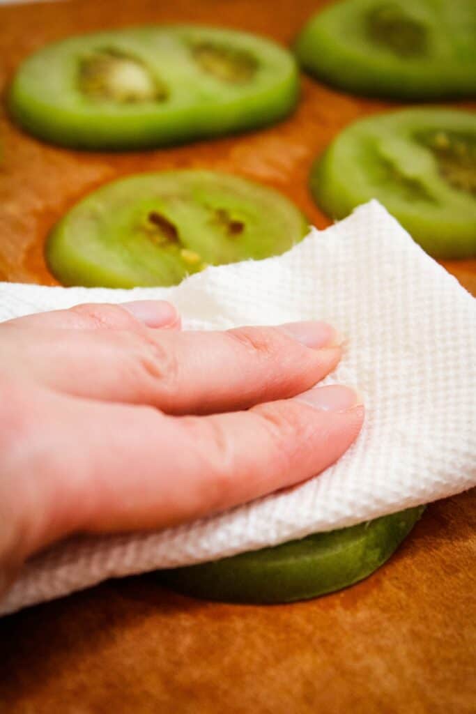 Green tomato being blotted dry with a paper towel.