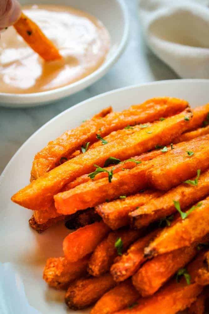 Air Fried Sweet Potato Fries on white plate with fry being dipped in sauce in background