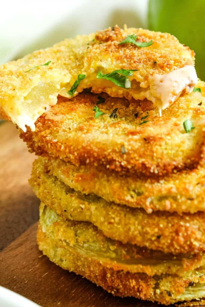 Stacked air fryer green tomatoes with a bite taken out of the top one.